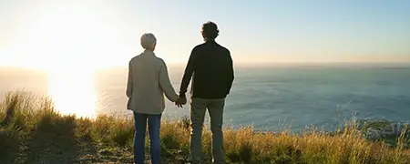 Ein Paar, das am Meer steht und sich an den Händen hält, während die Sonne untergeht