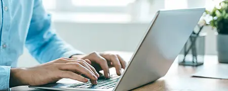 Nahaufnahme von Händen, die auf einer Laptop-Tastatur tippen